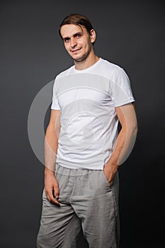 A handsome young man in a white t-shirt stands on a gray background. mockup