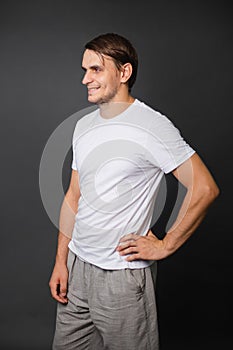 A handsome young man in a white t-shirt stands on a gray background. mockup