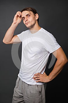 A handsome young man in a white t-shirt stands on a gray background. mockup