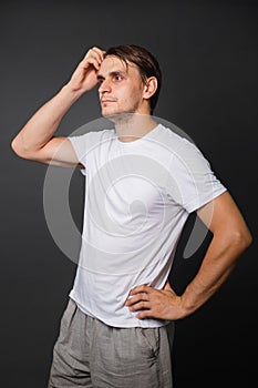 A handsome young man in a white t-shirt stands on a gray background. mockup