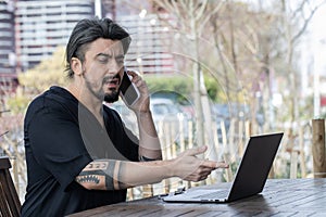 Handsome young man working on a laptop while on the phone