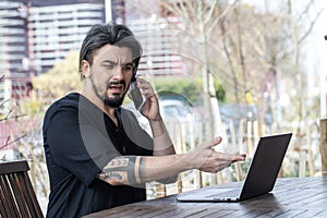 Handsome young man working on a laptop while on the phone