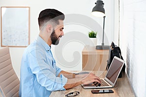 Handsome young man working with laptop at table in home