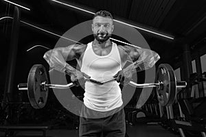 Handsome young man working out with a barbell in the gym. Shoulder pumping. Barbell pull to the chin