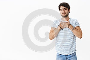Handsome young masculine guy with blue eyes sincerely sympatizing friend holding hands on breast pursing lips and gazing