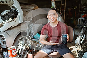 Handsome young mechanic shows a cell phone screen in an old garage