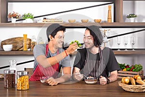 Handsome young men having breakfast together, one man feeding cereal to the other in modern dining room apartment on weekend.