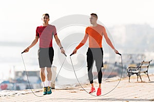 Handsome young men wearing sportswear and skipping rope at quay