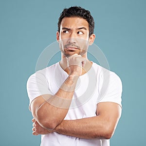 Handsome young mixed race man looking thoughtful with his hand on his chin and looking away while standing in studio