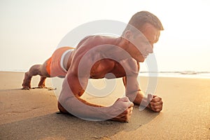 Handsome young muscular male model doing the workout stretching warm up on the beach summer.sexy athlete abs and perfect