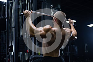 Handsome young muscular man of model appearance working out training pumping up back muscles in the gym gaining weight