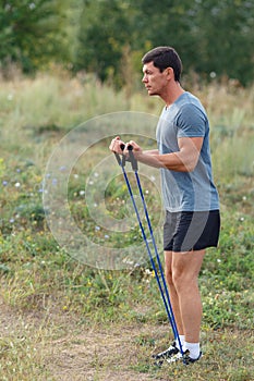 Handsome young muscular sports man exercising outside outdoor with rubber band.