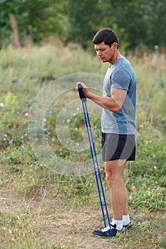 Handsome young muscular sports man exercising outside outdoor with rubber band.