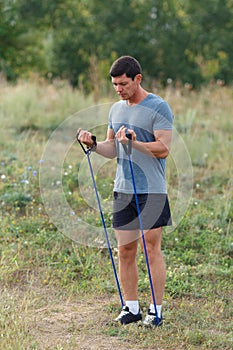 Handsome young muscular sports man exercising outside outdoor with rubber band.