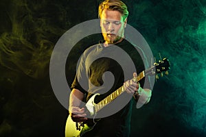 Handsome young musician man playing on guitar and singing in the smoke on stage or scene.