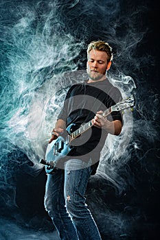 Handsome young musician man playing on guitar and singing in the smoke on stage or scene.