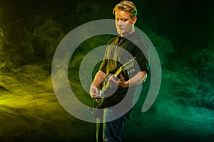 Handsome young musician man playing on guitar and singing in the smoke on stage or scene.