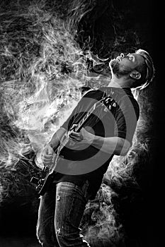 Handsome young musician man playing on guitar and singing in the smoke on stage or scene.