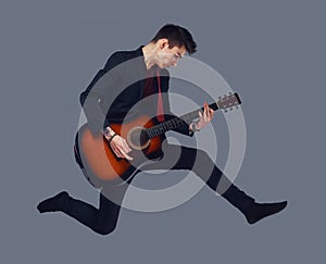 Handsome young musician playing guitar while jumping.