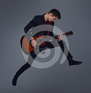 Handsome young musician playing guitar while jumping.