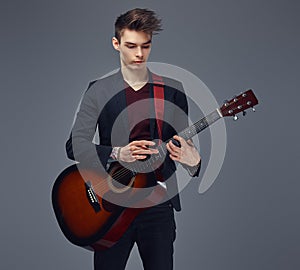 Handsome young musician with stylish hair in elegant clothes, playing on an acoustic guitar.