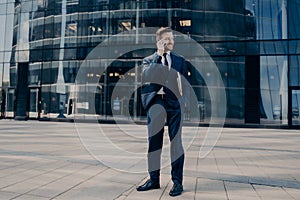 Handsome young office worker in dark blue formal suit speaks on cellphone