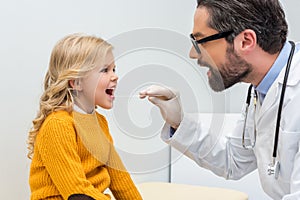 handsome young pediatrist checking throat of adorable