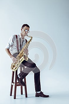 handsome young performer sitting on stool and playing saxophone