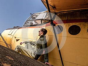 A handsome young pilot sitting on the wing of a plane