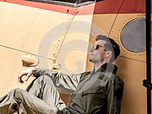 A handsome young pilot sitting on the wing of a plane