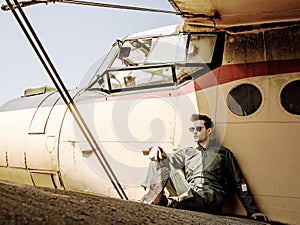 A handsome young pilot sitting on the wing of a plane