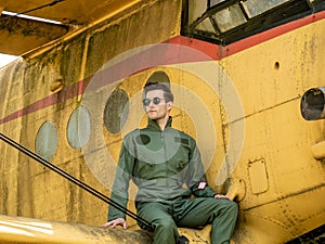 A handsome young pilot sitting on the wing of a plane