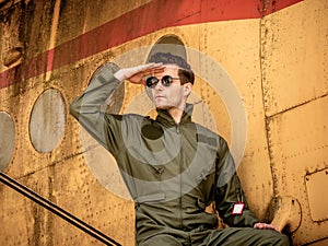 A handsome young pilot sitting on the wing of a plane and covering the sun