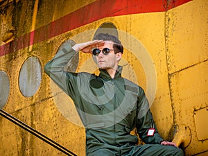 A handsome young pilot sitting on the wing of a plane and covering the sun