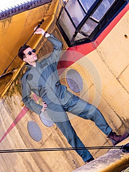 A handsome young pilot standing on the wing of a plane