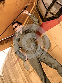 A handsome young pilot standing on the wing of a plane