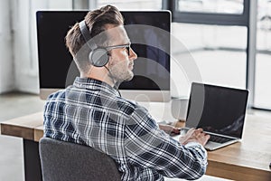 handsome young programmer in eyeglasses and headphones working with laptop