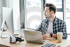 handsome young programmer using laptop and desktop computer