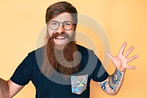 Handsome young red head man with long beard wearing casual clothes and glasses celebrating victory with happy smile and winner