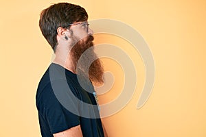 Handsome young red head man with long beard wearing casual clothes and glasses looking to side, relax profile pose with natural