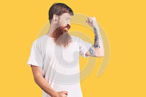 Handsome young red head man with long beard wearing casual white tshirt showing arms muscles smiling proud