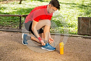 Handsome young runner tying shoelaces on the track in the spring park. Near him is an orange thermocouple