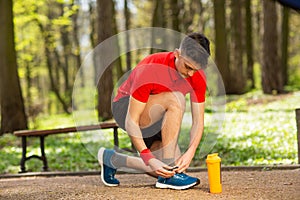 Handsome young runner tying shoelaces on the track in the spring park. Near him is an orange thermocouple