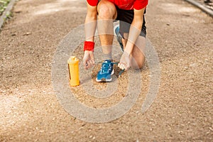 Handsome young runner tying shoelaces on the track in the spring park. Near him is an orange thermocouple