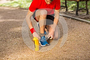 Handsome young runner tying shoelaces on the track in the spring park. Near him is an orange thermocouple