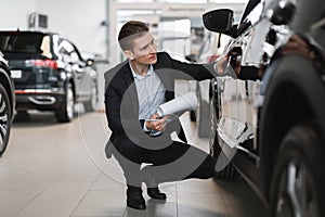 Handsome young sales manager making new automobile checkup at luxury car salon, full length