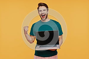 Handsome young smiling man in casual clothing carrying laptop and gesturing