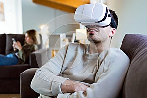 Handsome young smiling man using virtual reality headset at home.