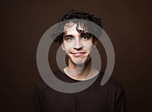 Handsome young smiling man wear brown t-shirt looking at camera on brown background