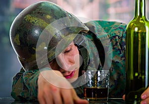 Handsome young soldier wearing uniform suffering from stress post-war, with a glass of ron and bottle next to him, in a